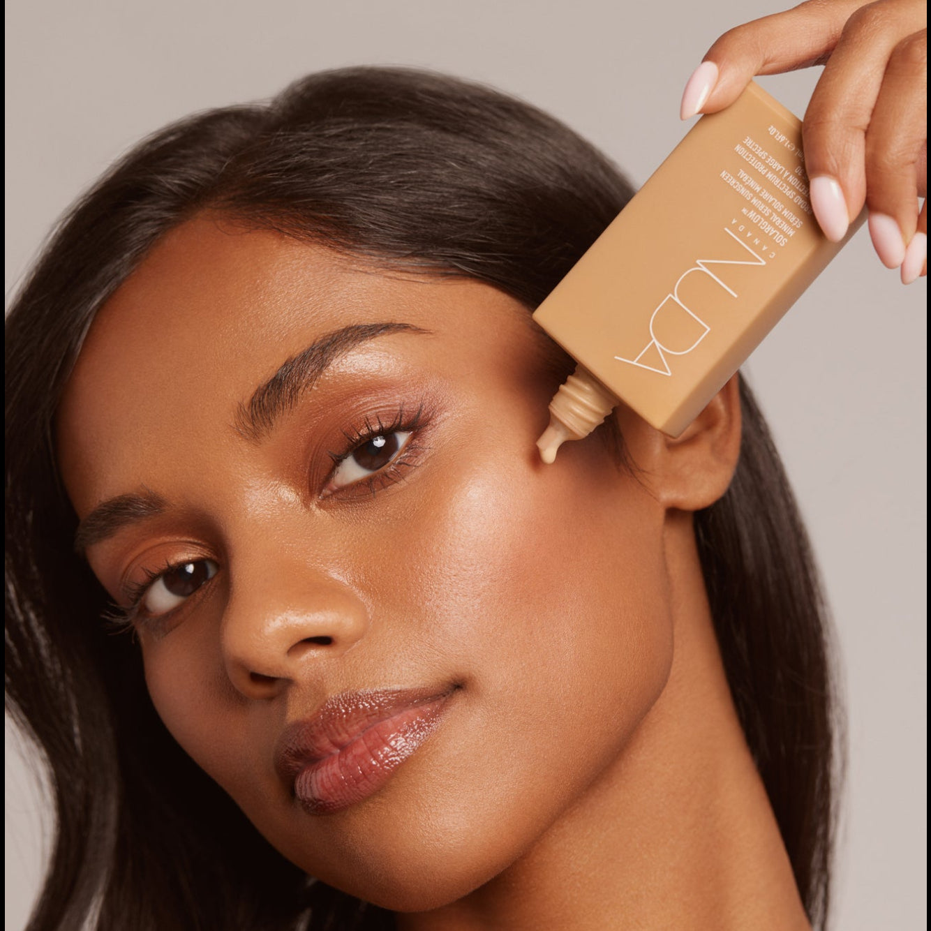 Woman applying foundation with a brush on a neutral background