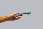 Hand holding a blue handheld massager against a gray background