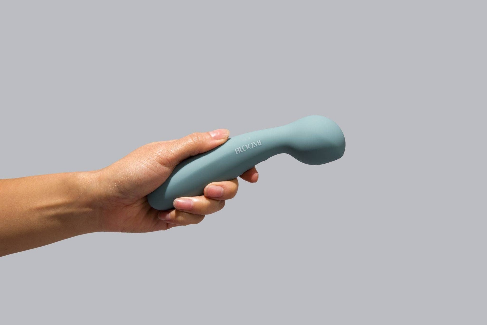 Hand holding a blue handheld massager against a gray background