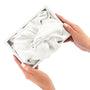 White silk bonnet in a box held by hands on a white background