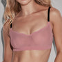 A woman wearing a dusty pink wireless bralette with thin black shoulder straps, shown from the chest up against a light gray background.