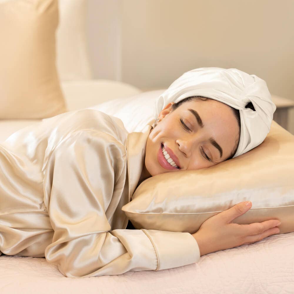 Woman in a robe with a silk white bonnet on her head, lying on a pillow in a spa setting.