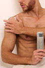 Man applying Think Rich Luxe Body Lotion to his shoulder holding a bottle on a white background. 