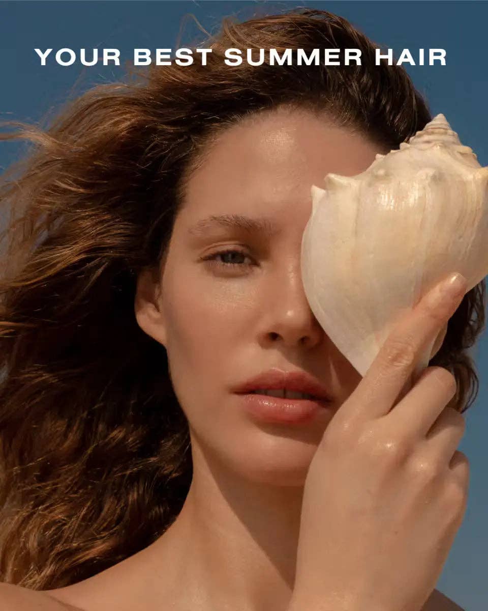 Woman holding a shell to her face with text 'Your Best Summer Hair' against a blue sky.