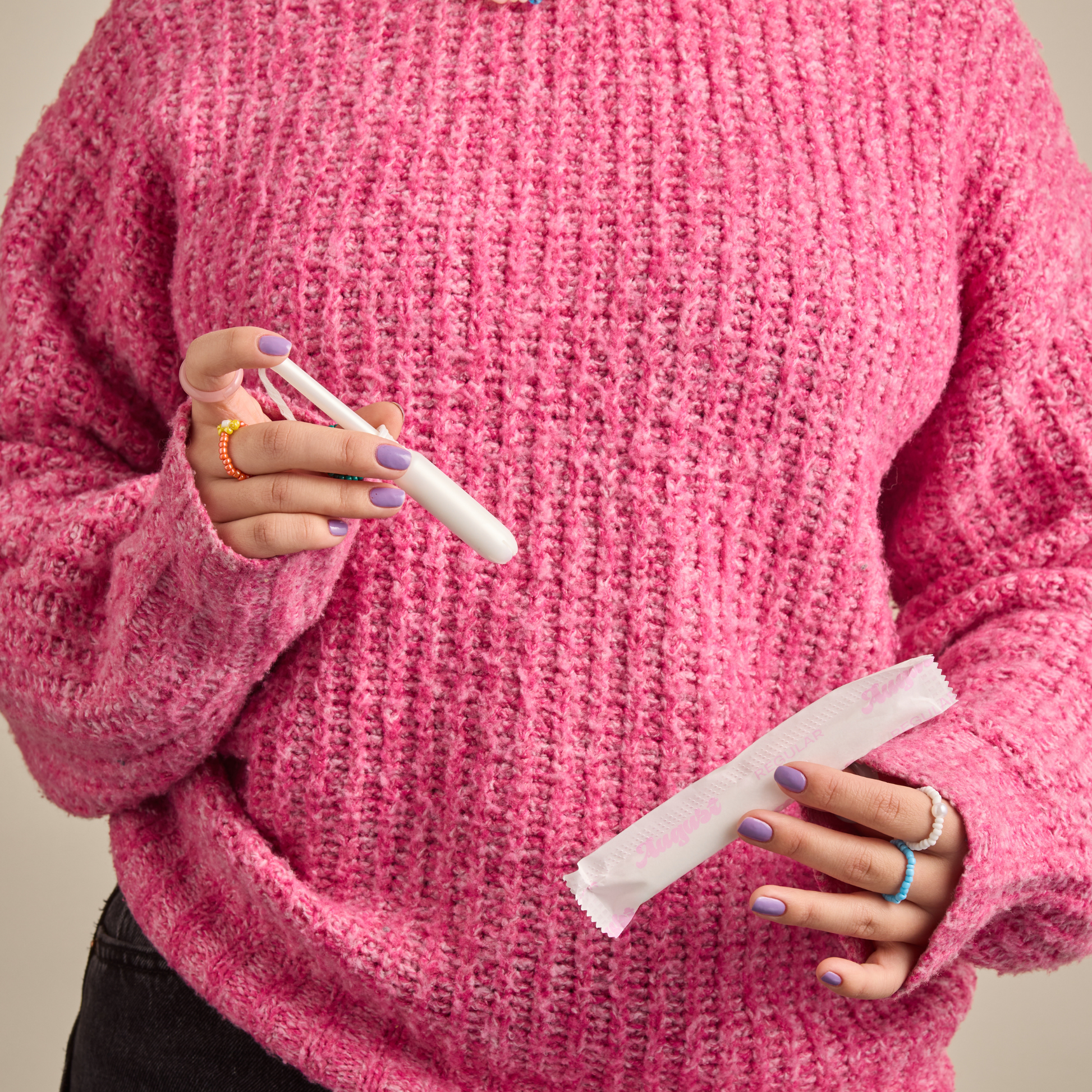 Person wearing a pink sweater holding a tampon out of the wrapper