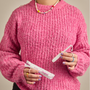 Person wearing a pink sweater holding a tampon out of the wrapper