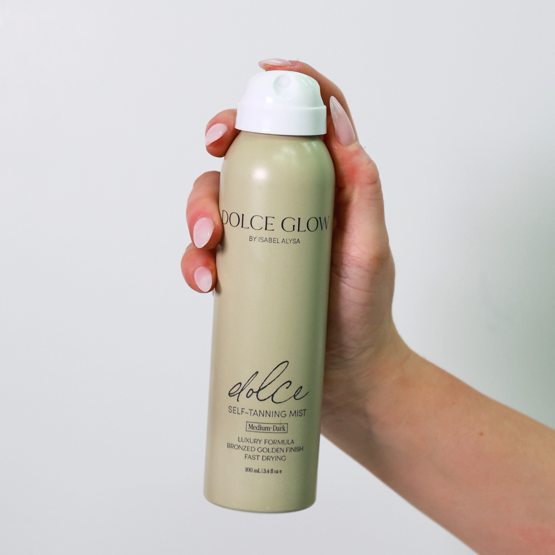Hand holding a Dolce Glow self-tanning mist bottle against a plain background