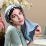 Woman wearing a satin bonnet in a home setting with flowers and a mirror in the background.