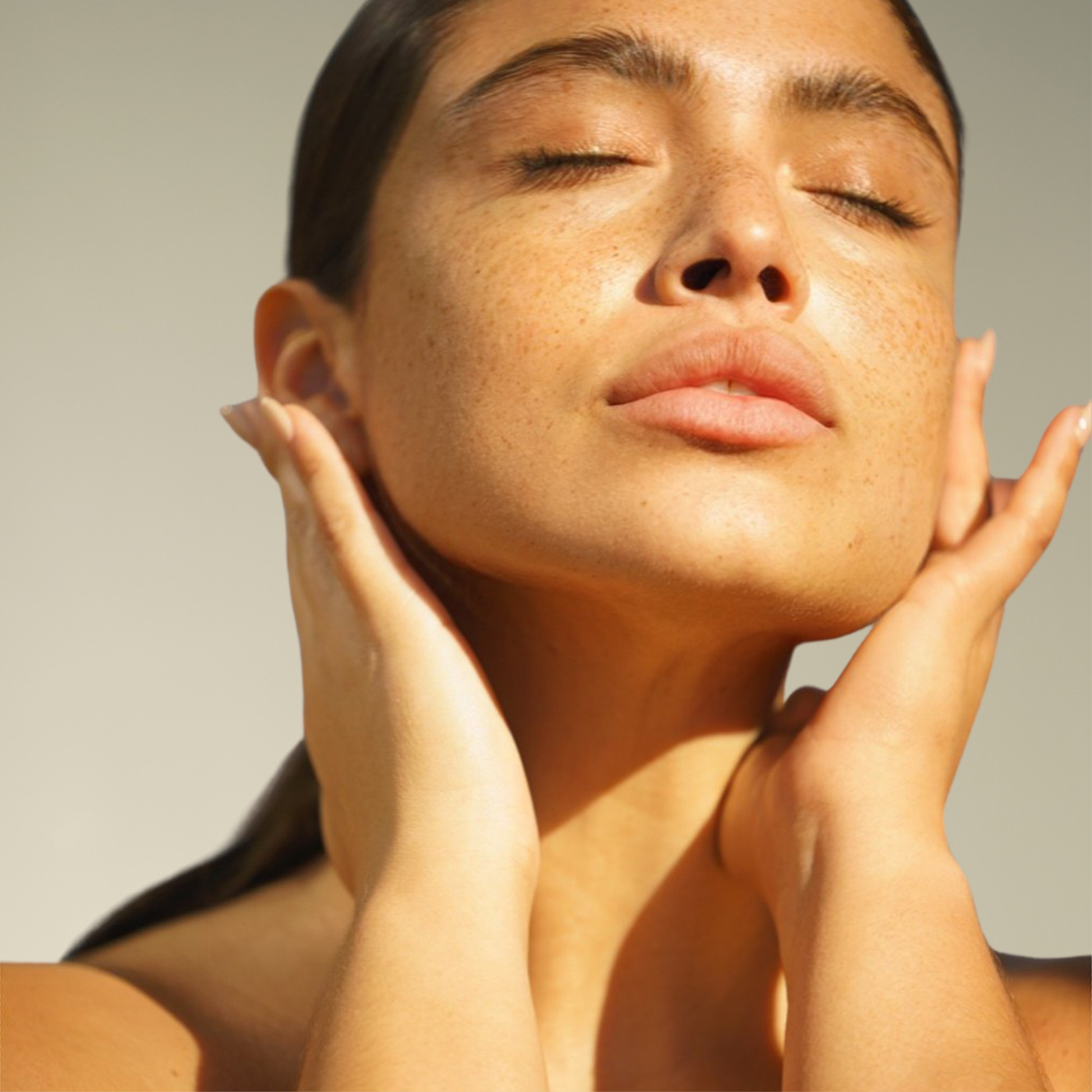 Woman with hands on face against a neutral background and glowing skin