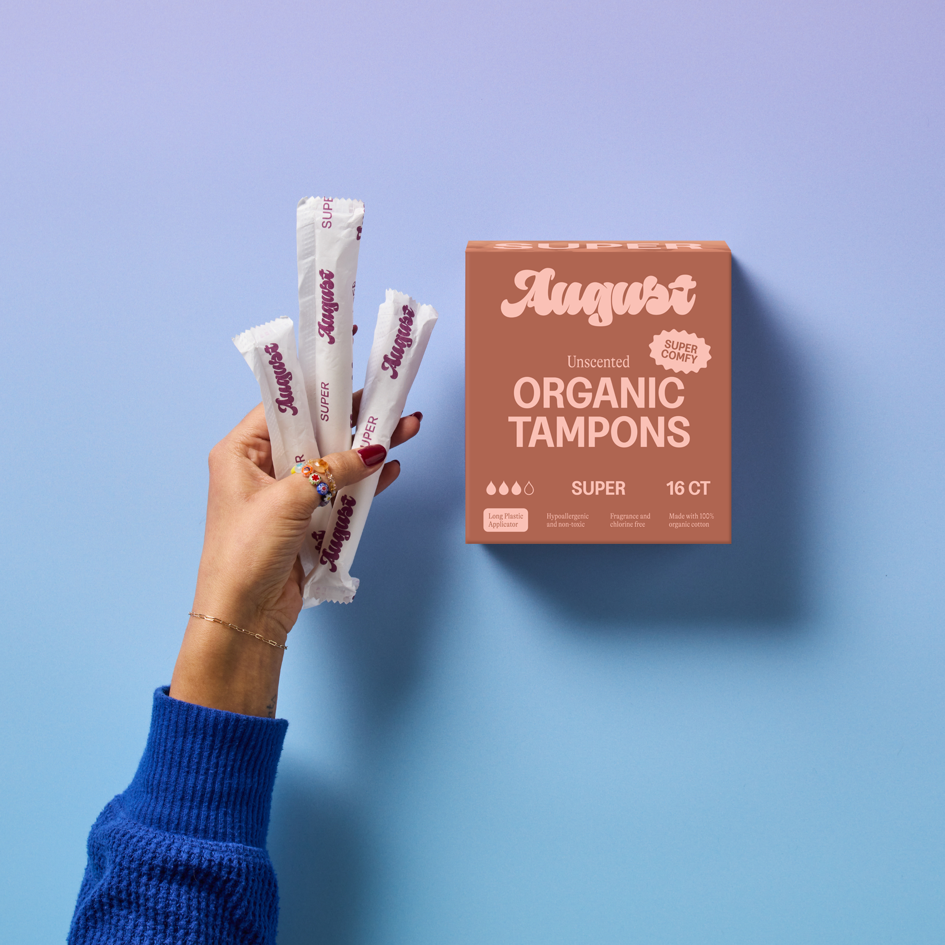 Hand holding August organic tampons against a blue background