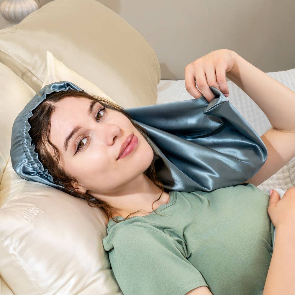 Woman using a blue satin hair cap while lying on a bed.