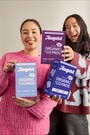 Two women holding packages of August organic cotton cover pads against a plain background