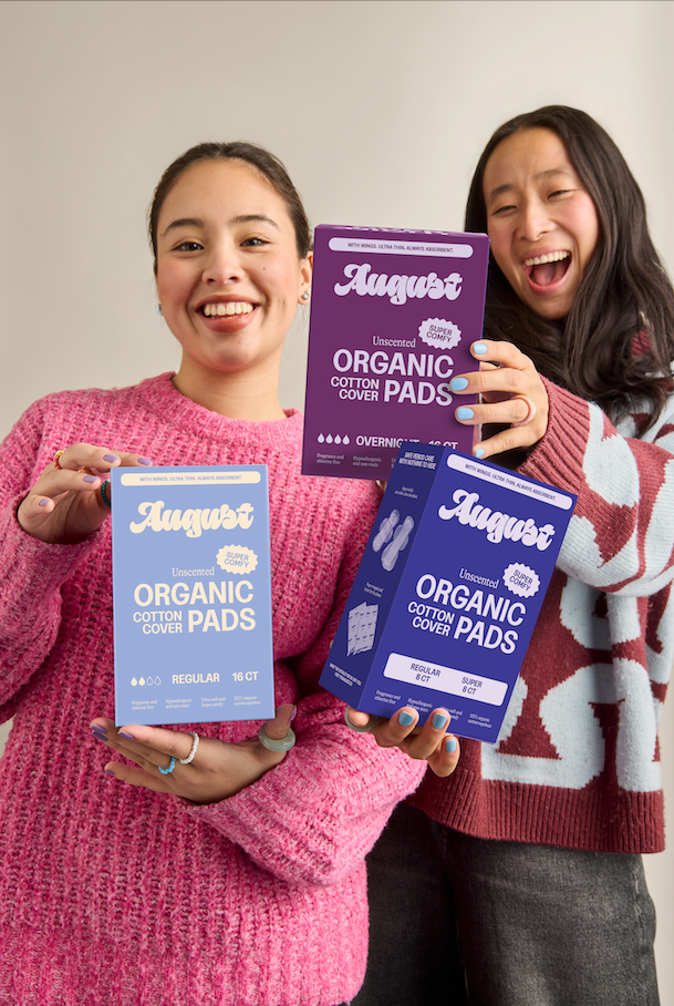 Two women holding packages of August organic cotton cover pads against a plain background