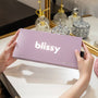 Person holding a laendar 'blissy' box in front of decorative bottles on a mirror.