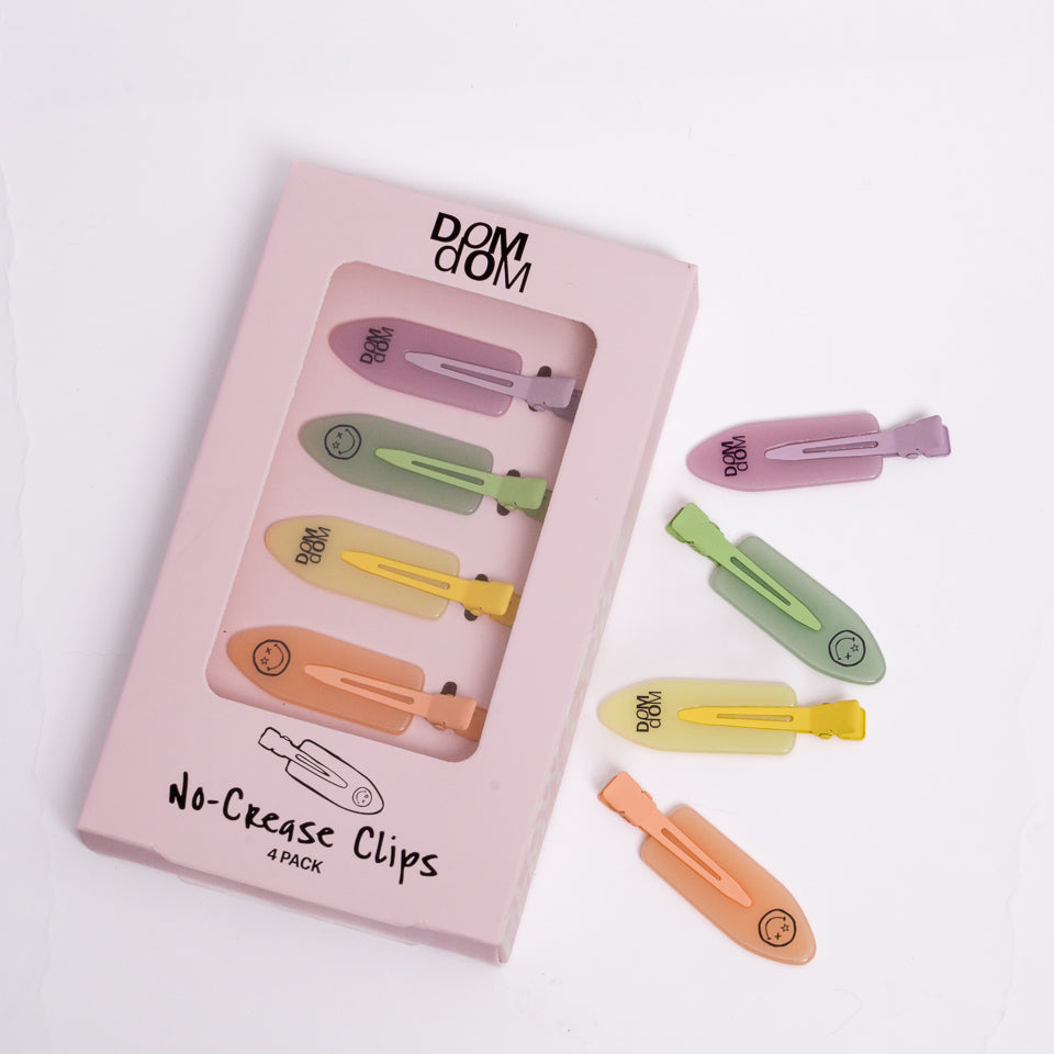 A 4-pack of pastel no-crease hair clips by Dom Dom, shown in their pink packaging box with three loose clips displayed to the right on a clean white background.