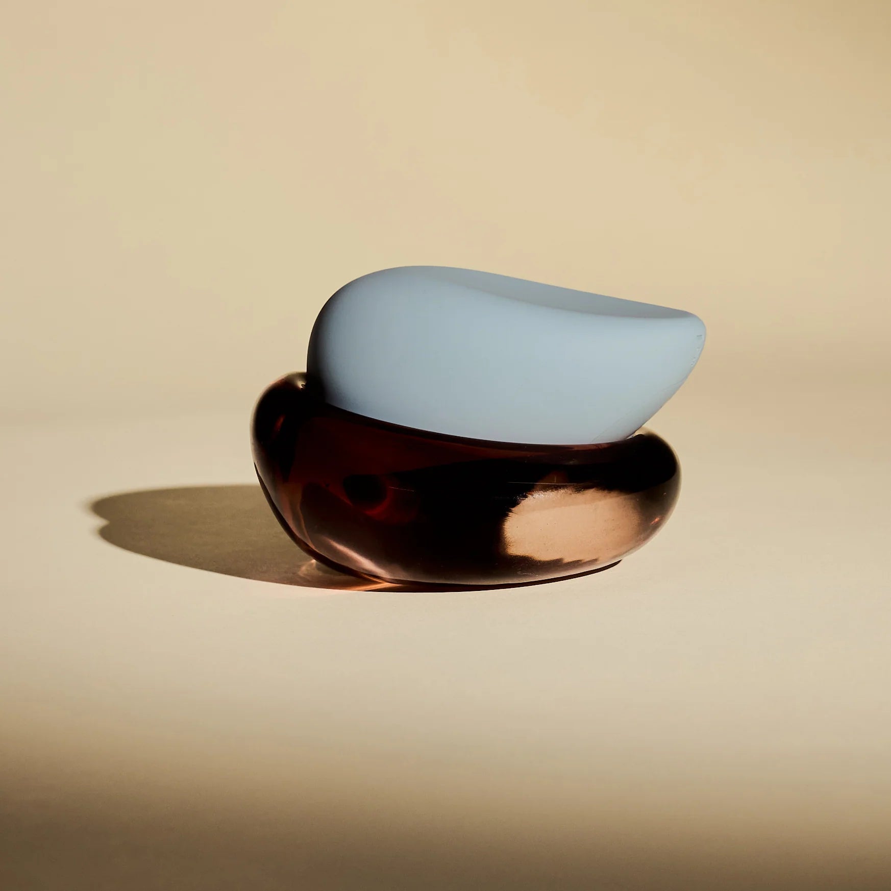Modern brown dish with a glossy finish on a beige background with blue personal massager sitting atop.