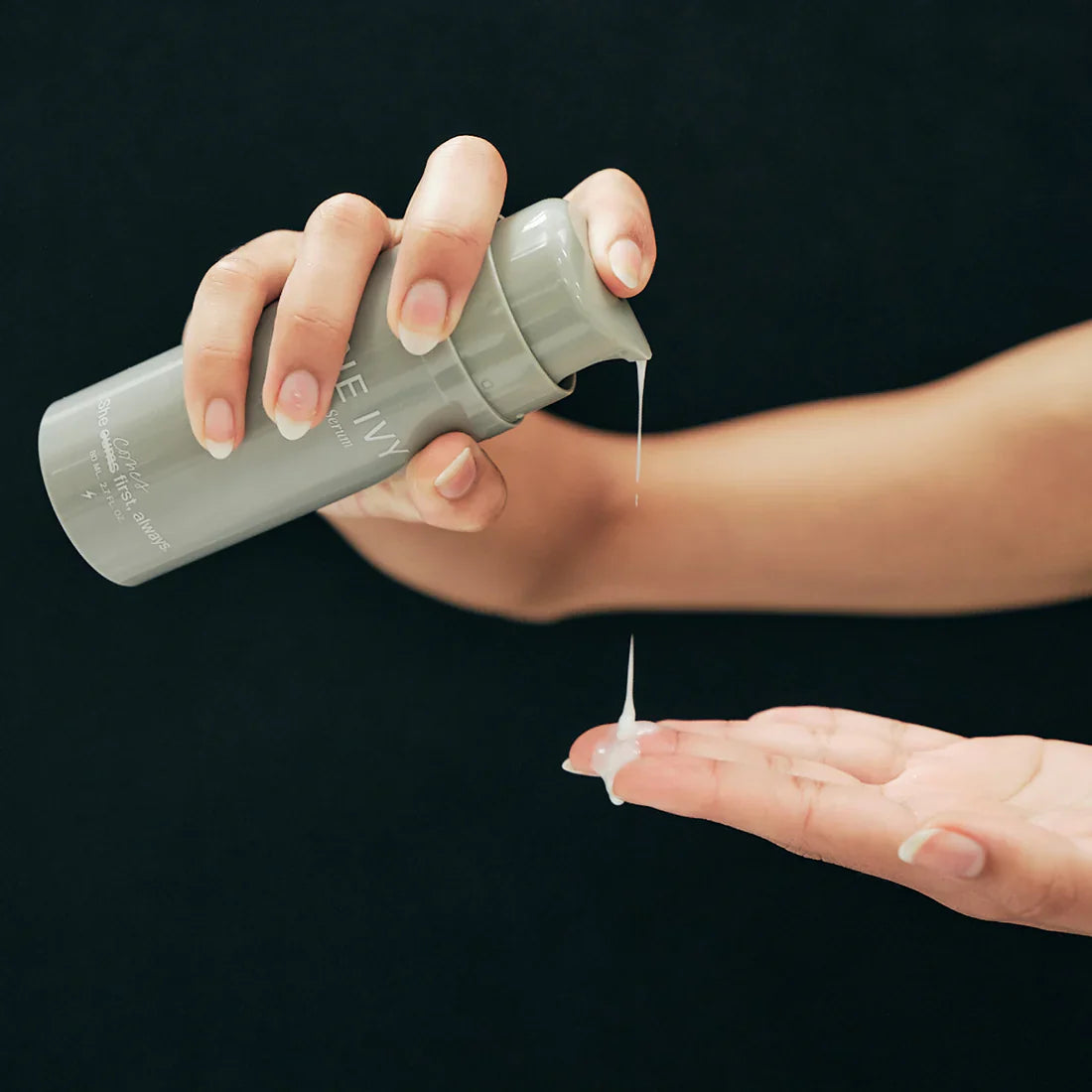 Person holding a gray bottle of skincare product with black background