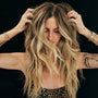 Woman with long, wavy hair adjusting her hair against a black background