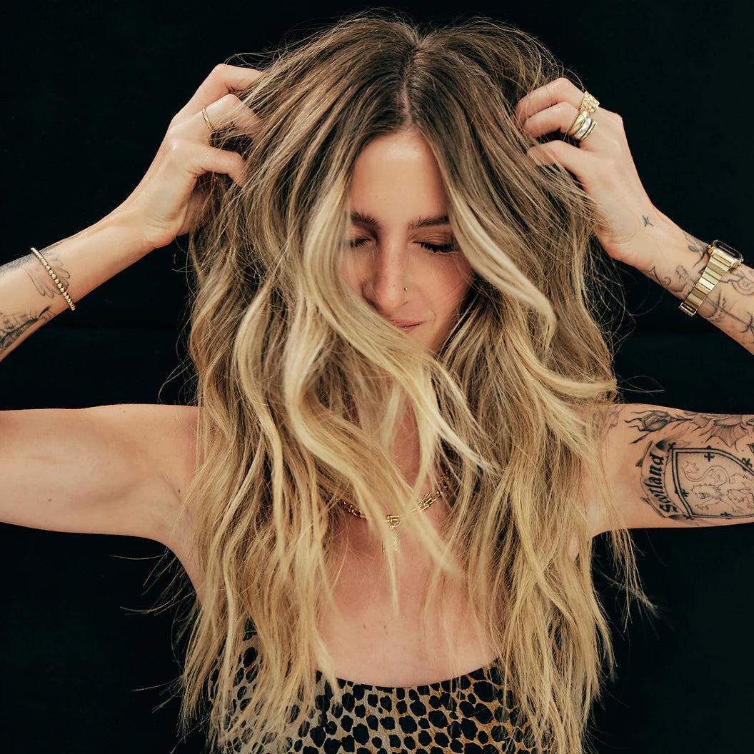 Woman with long, wavy hair adjusting her hair against a black background