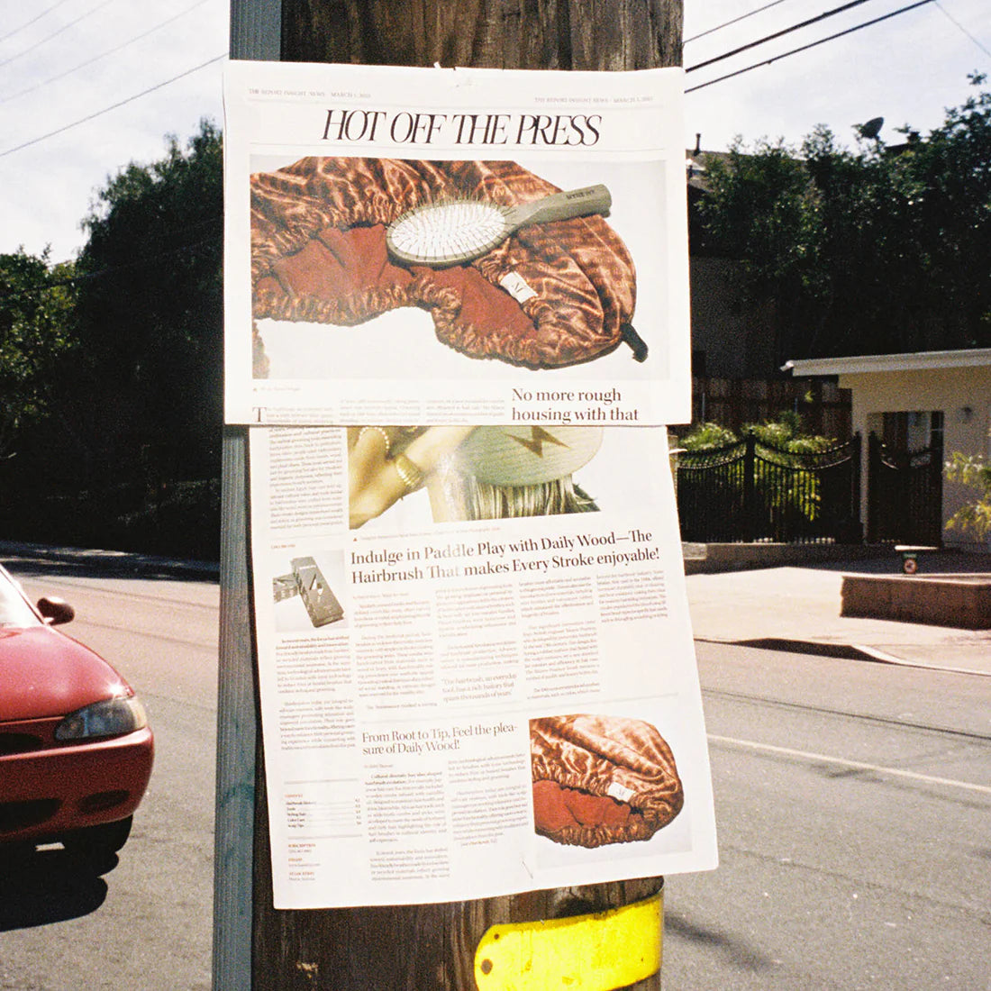 Advertisement for Daily Wood hairbrushes on a utility pole with a street and car in the background.