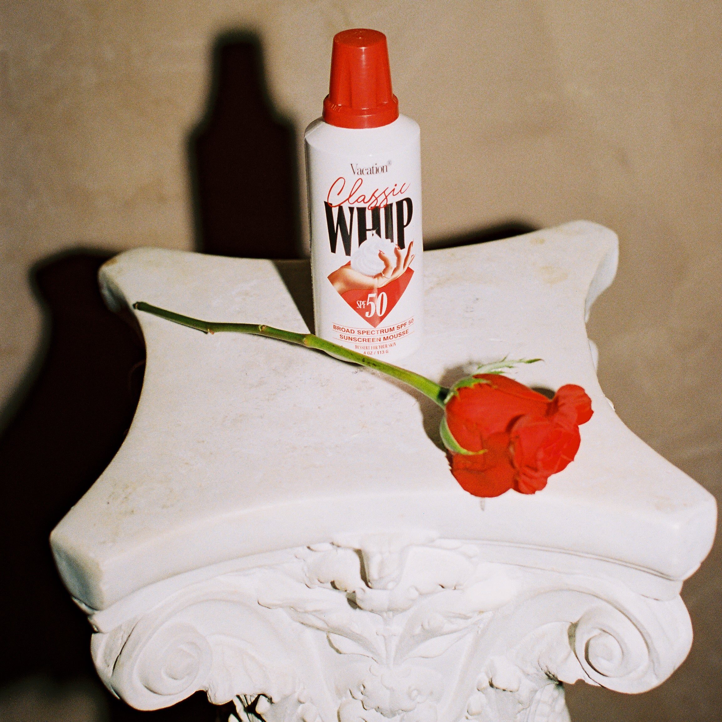 classic whip sunscreen on a pedestal with a rose against a beige background