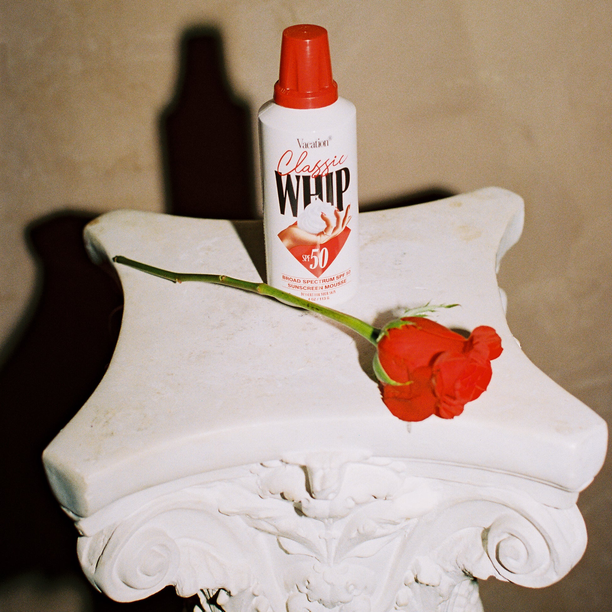 classic whip sunscreen on a pedestal with a rose against a beige background