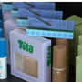 Tita boxes displayed in a retail or storage setting, with a white box featuring a clear window showing beige single covers, blue and green product boxes, and brown cylindrical containers.