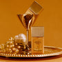 Gold bottle of 'Vacation Summer Oil SPF 30' on a tray with grapes and a glass against an orange background