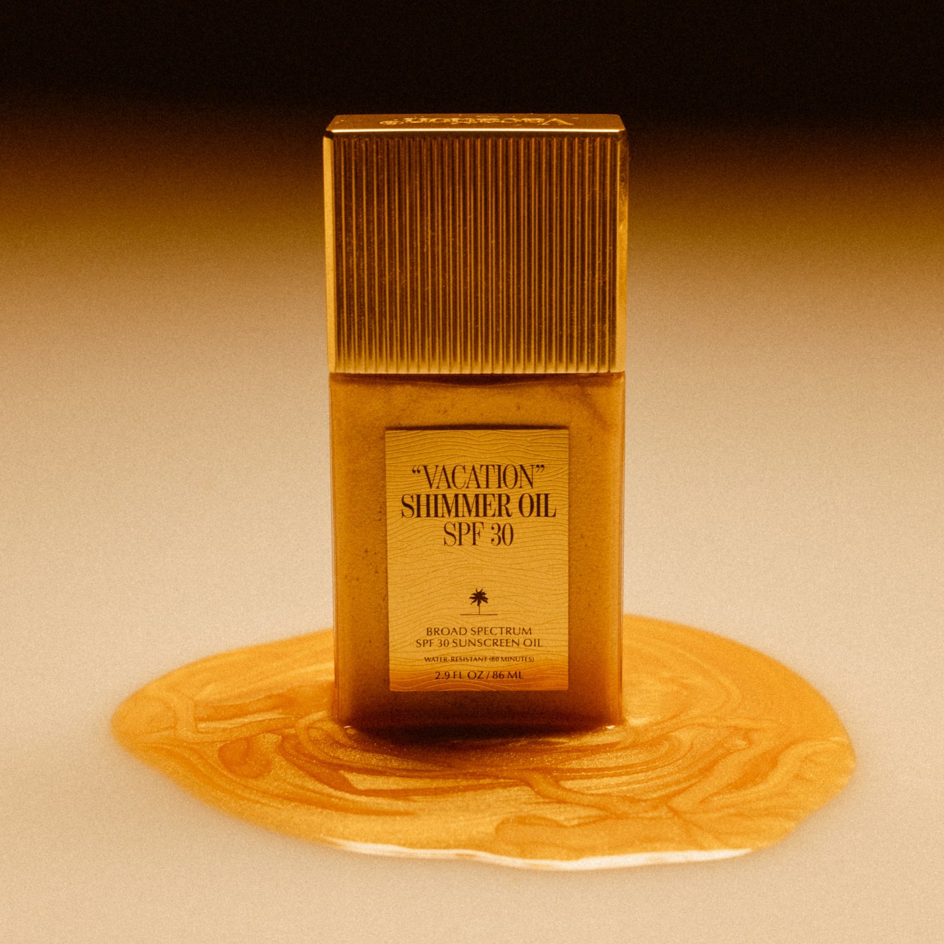 Gold bottle of 'Vacation Shimmer Oil SPF 30' on a beige background