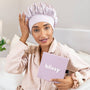 Woman wearing a satin bonnet and holding a 'blissy' product box in a bedroom setting.