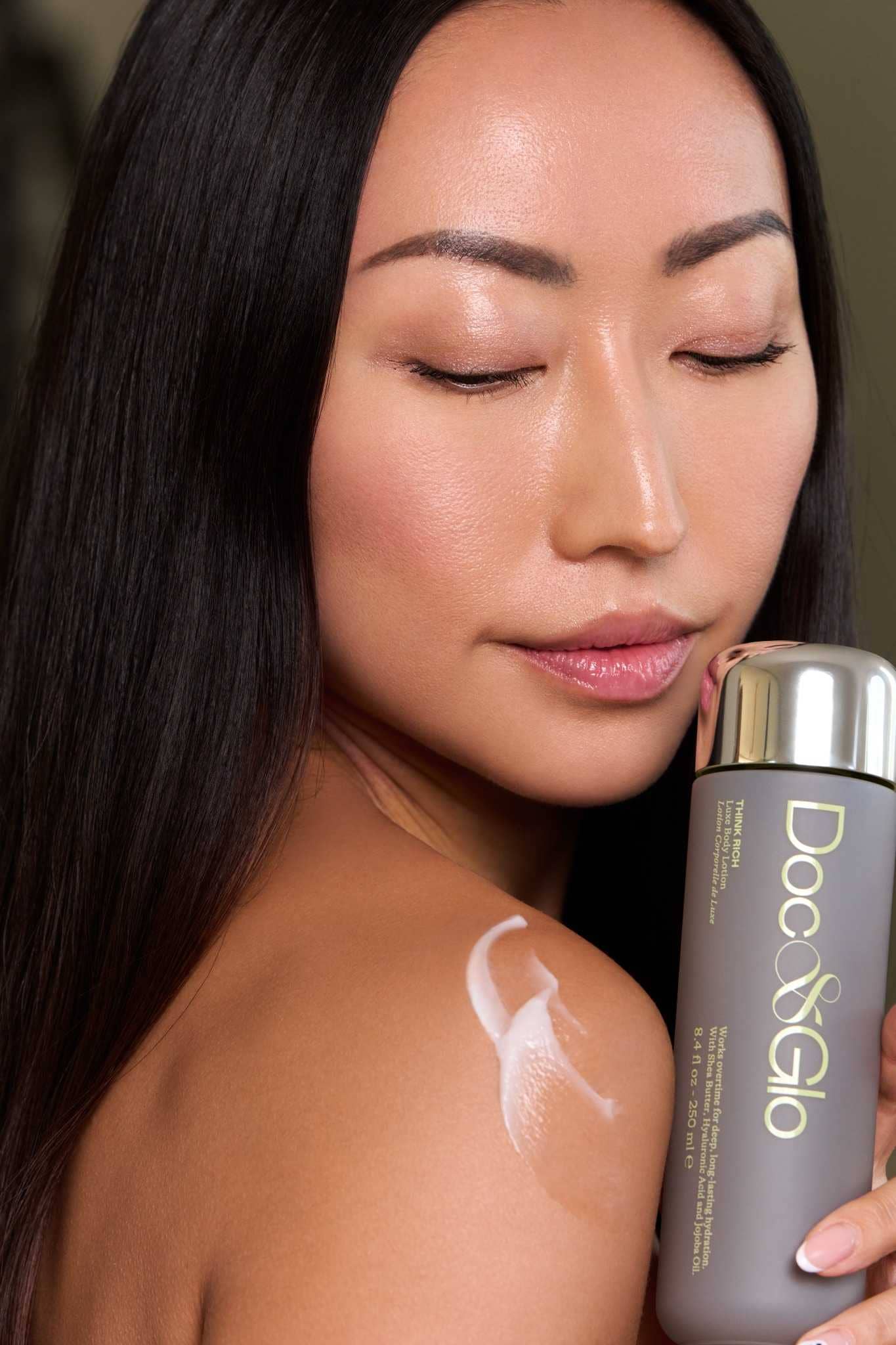 Woman applying think rich luxe body lotion to her shoulder holding a bottle against her shoulder. 