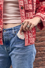 Person wearing a red patterned jacket and blue jeans with a brick wall background pulling a panty liner out of their pocket