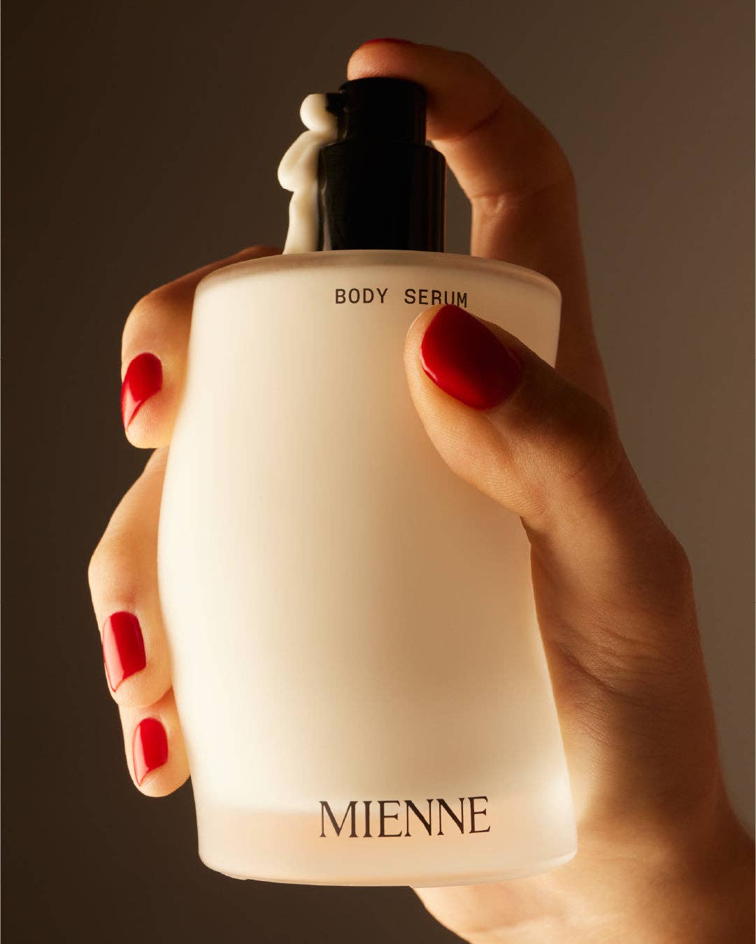 Hand holding a Mienen body serum bottle against a dark background