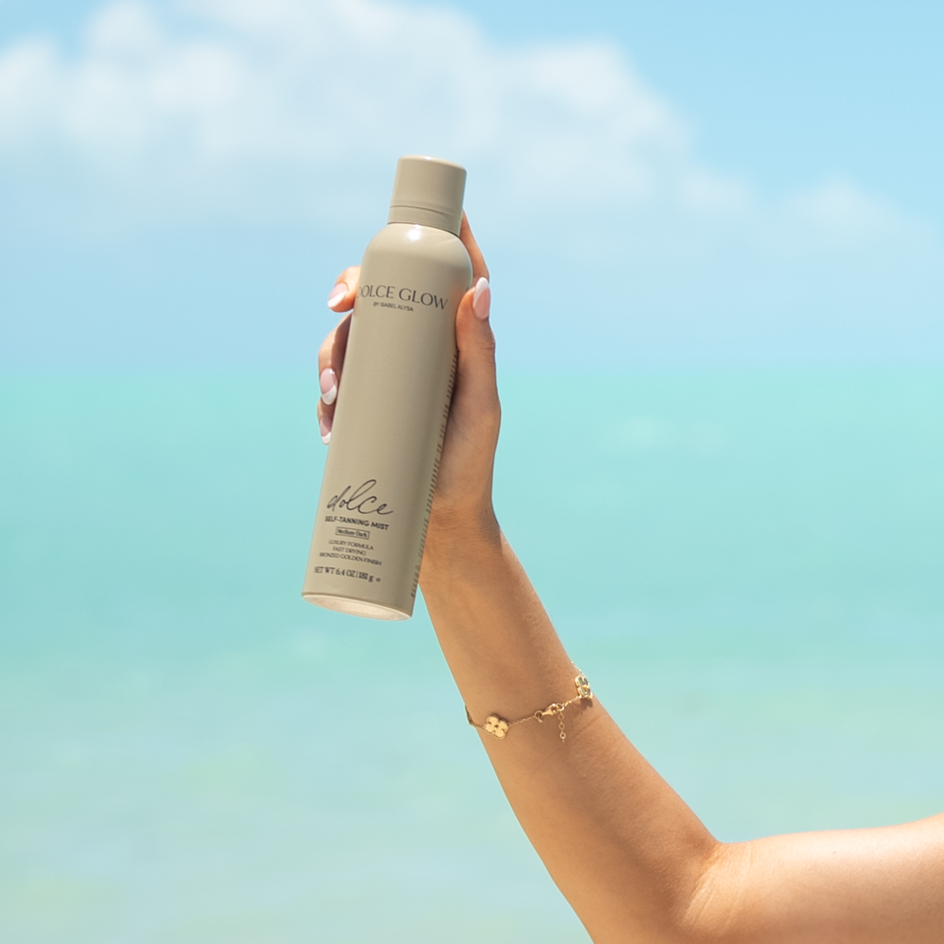 Hand holding a bottle of 'Dolce Glow' product against a gradient blue background