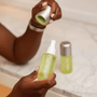 Person holding a green spray bottle with a silver cap in a bathroom setting