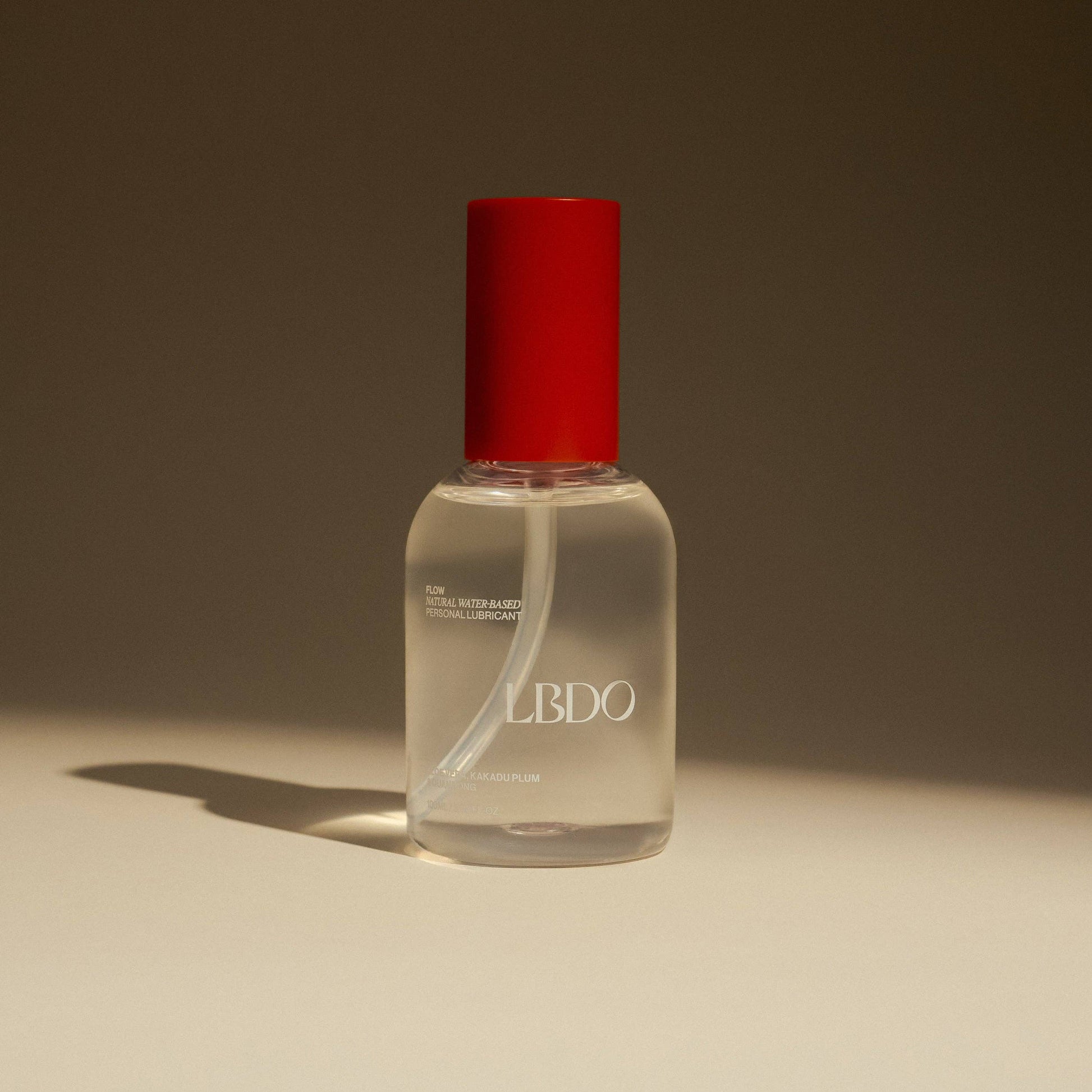 Clear bottle with red cap on a beige surface and brown background