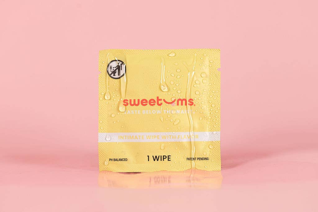 Yellow sweetums wipe on a pink background with water droplets on the pack