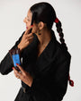 Model holding Ceremonia Pequi styling gel bottle for frizz control and using cermonia brush to tame ponytail.