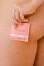 Pink sweetums wipe packaging held by a hand on a person's leg