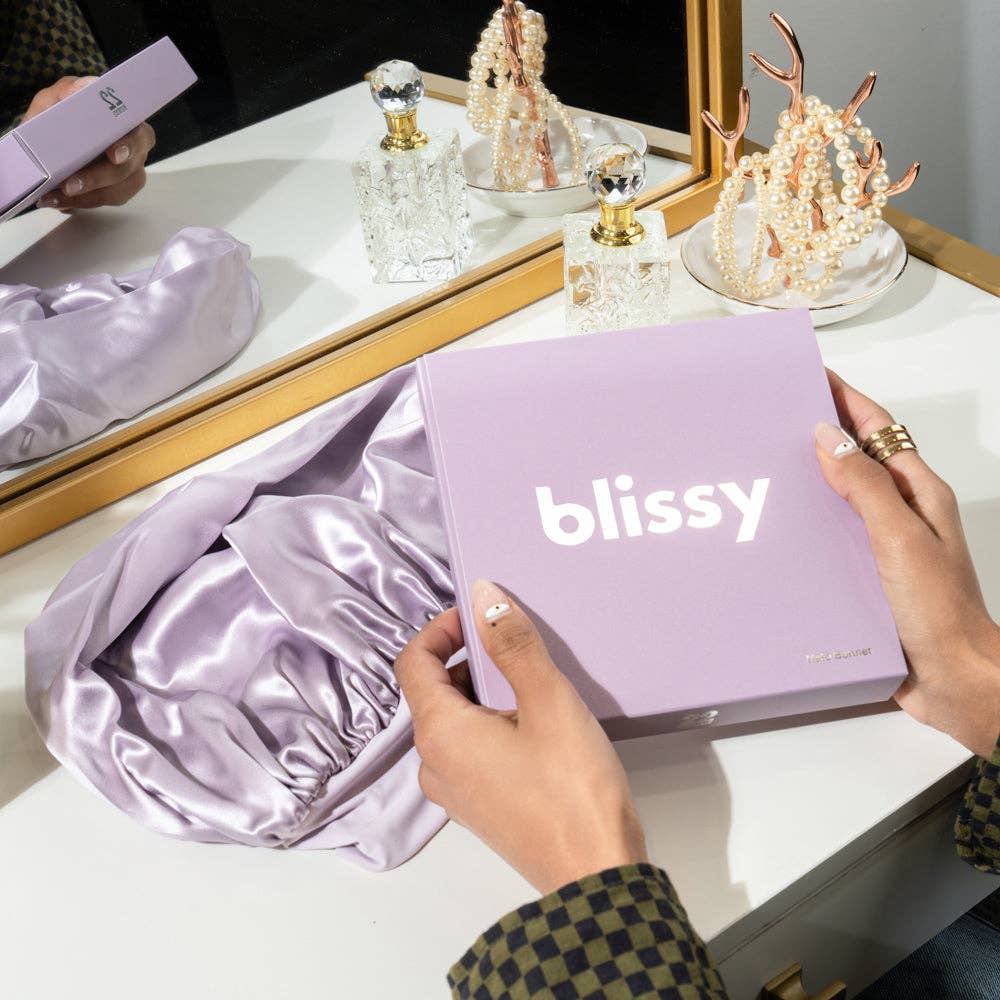 Person holding a 'blissy' product box with jewelry and satin fabric in the background.