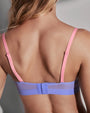 Close-up back view of a woman wearing a bra with thin pink straps and a lavender-blue underband and mesh back panel.