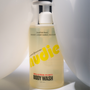 Bottle of Nudie body wash with a white pump on a light background
