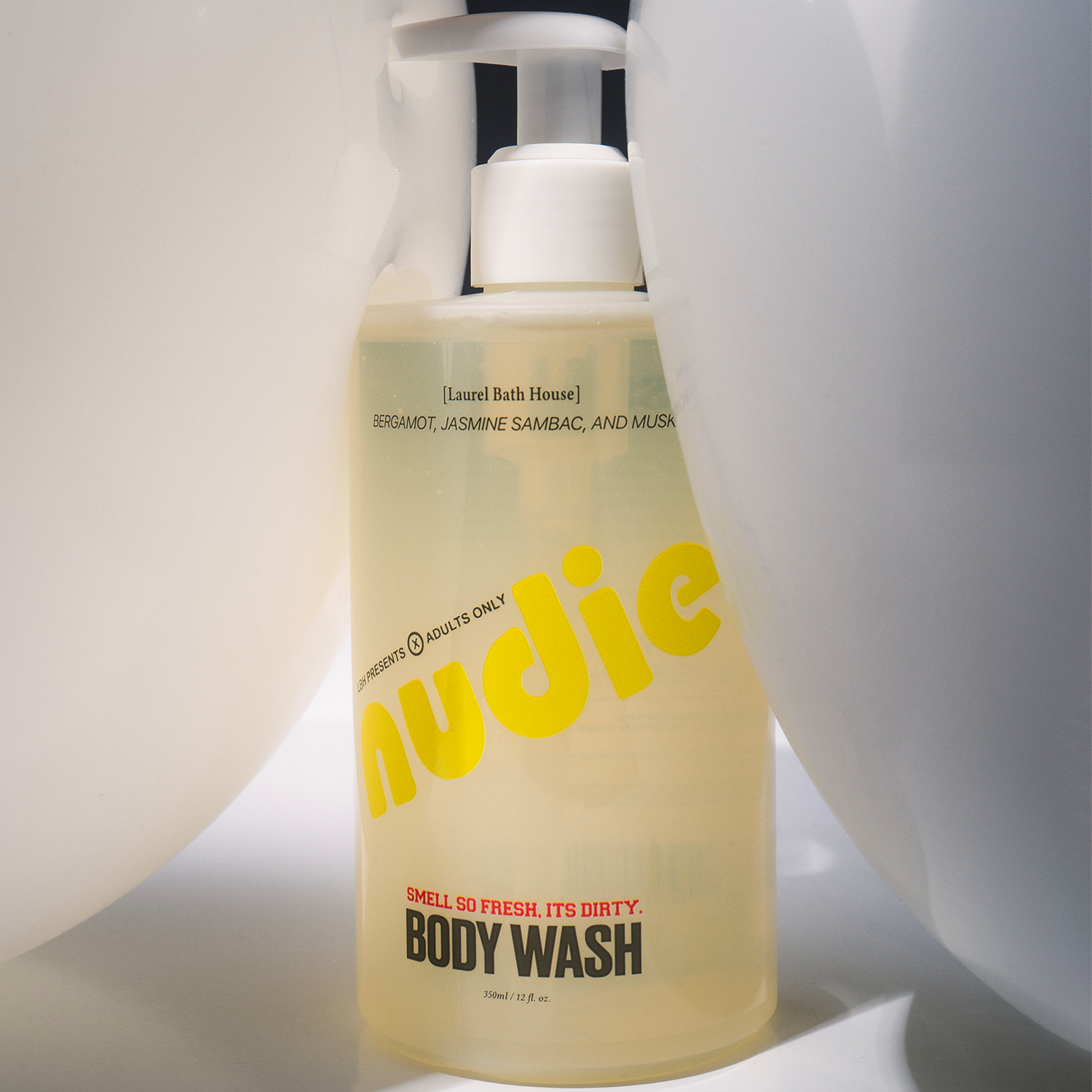Bottle of Nudie body wash with a white pump on a light background