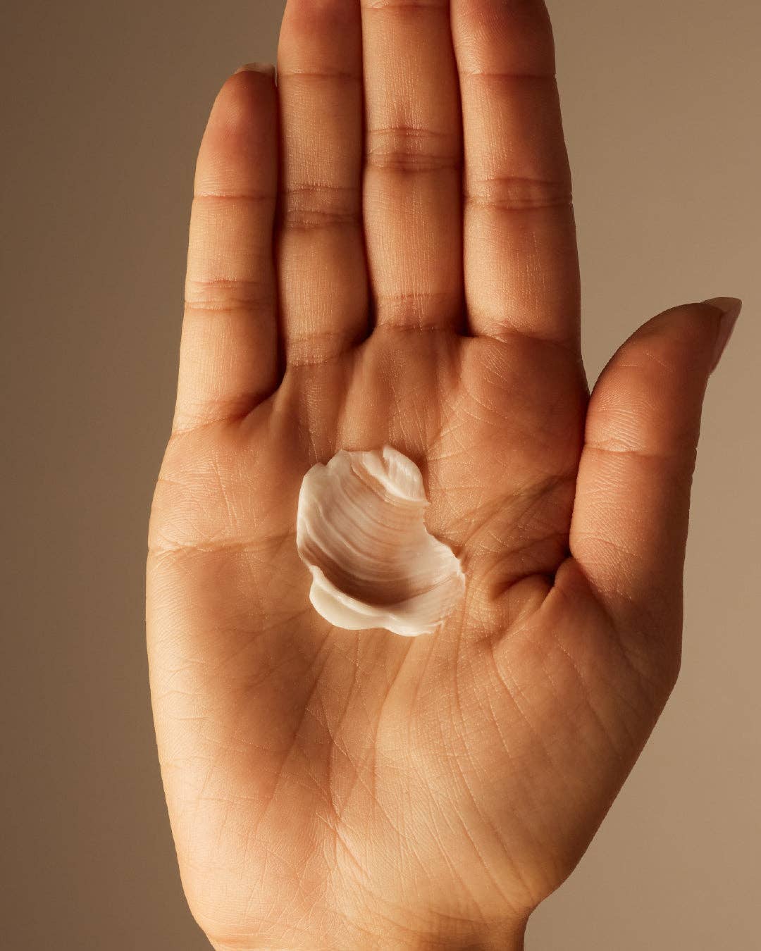 Hand holding cream against a brown background