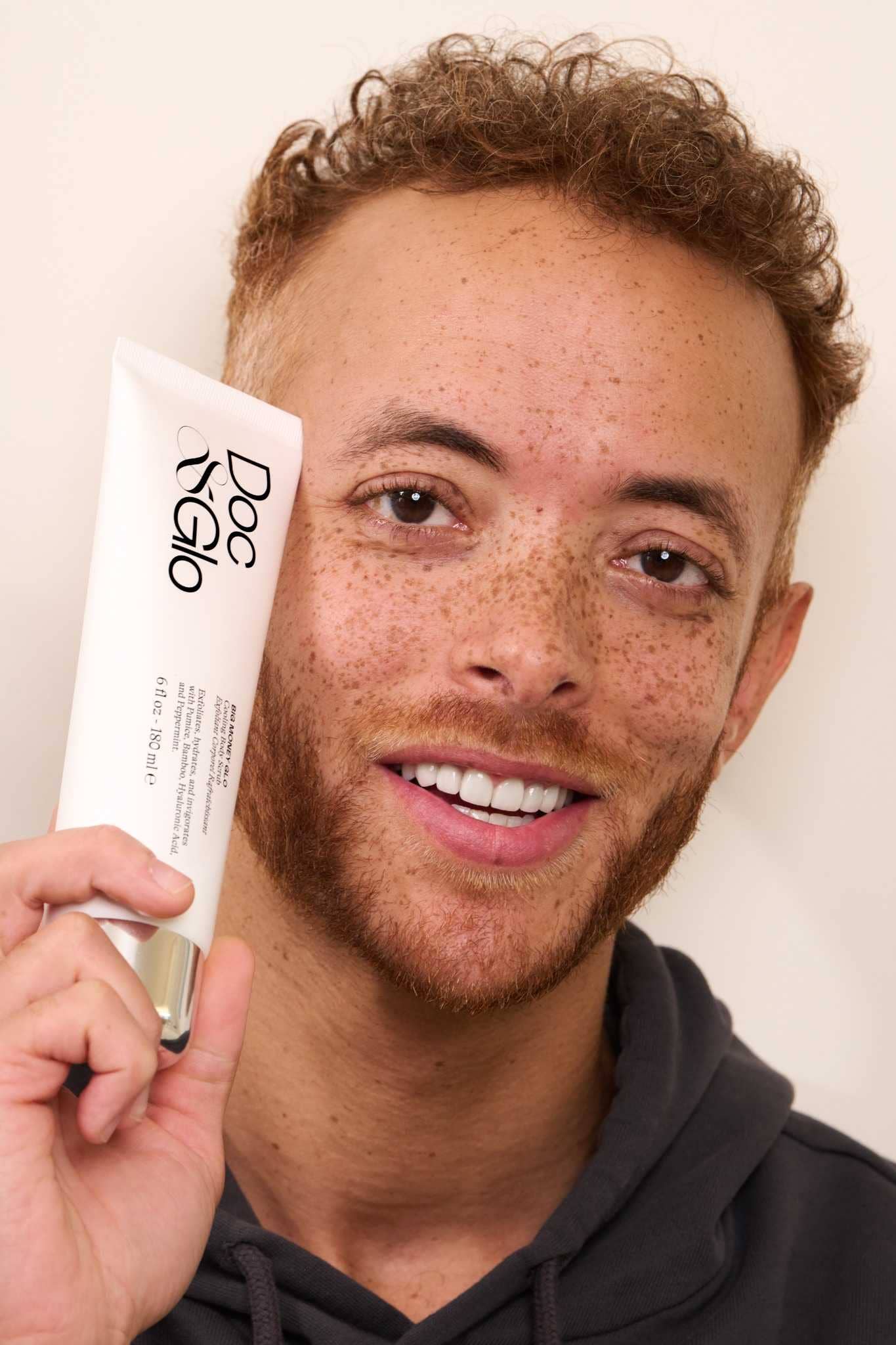 Man holding Big Money Glo Cooling Body Scrub product with a neutral background