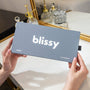 Person holding a 'blissy' product packaging in front of a mirror with decorative items.