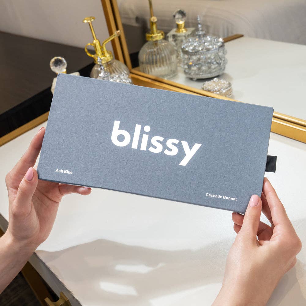 Person holding a 'blissy' product packaging in front of a mirror with decorative items.