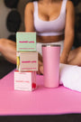 Sweetums boxes and a pink tumbler on a pink mat with a blurred person in the background on a yoga mat.