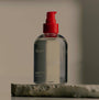 Clear bottle with red pump top on a stone surface against a neutral background