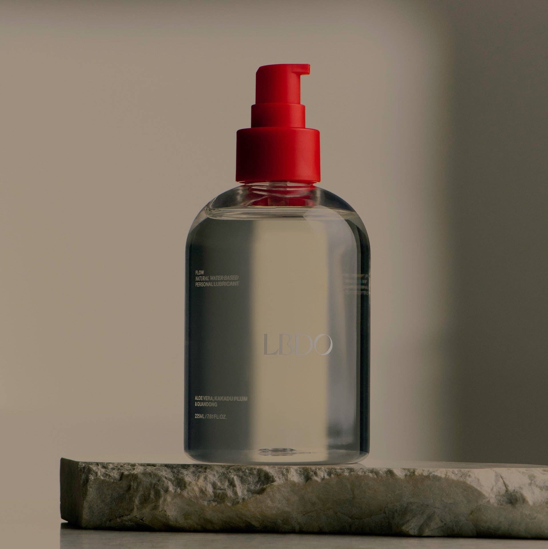 Clear bottle with red pump top on a stone surface against a neutral background